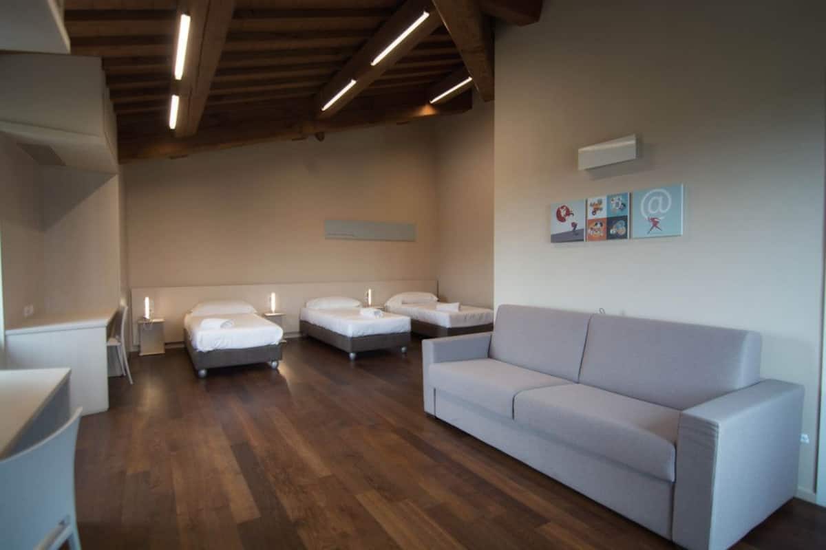 Een moderne hotelkamer met een houten plafond, een grijze bank, twee enkele bedden, een bureau en een kleine tafel.