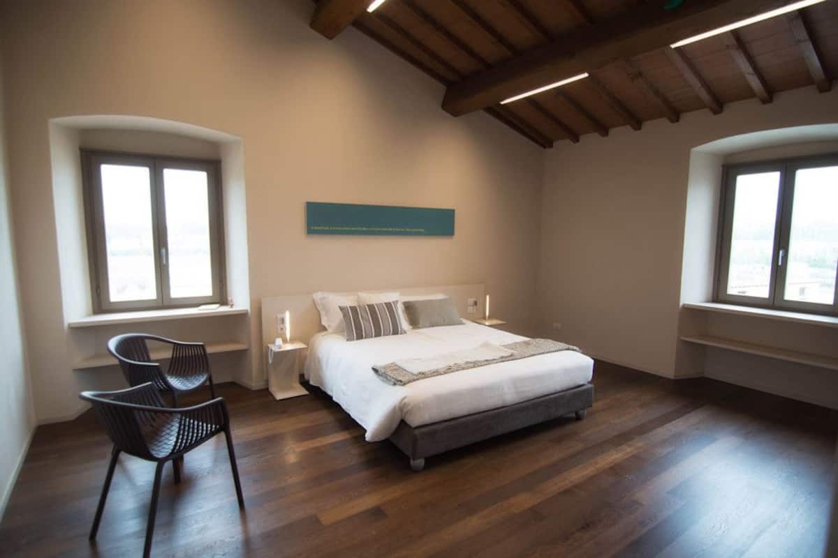 Een slaapkamer met een groot bed, twee nachtkastjes, een stoel en twee ramen.