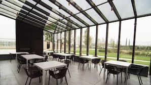 An outdoor patio area with tables and chairs, large windows, and a view of the landscape.