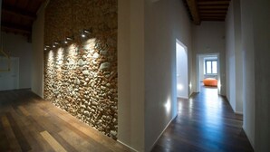 A hallway with a stone wall and wooden flooring, leading to a door and a bright room with an orange chair.