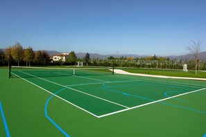 Un court de tennis en plein air, avec un ciel dégagé et des montagnes en arrière-plan.