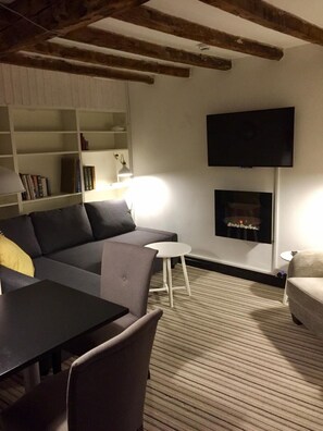 A cozy living room with a sofa, a small table, a bookshelf, and a fireplace. - Greenbank Lodge Llangollen (Llangollen)