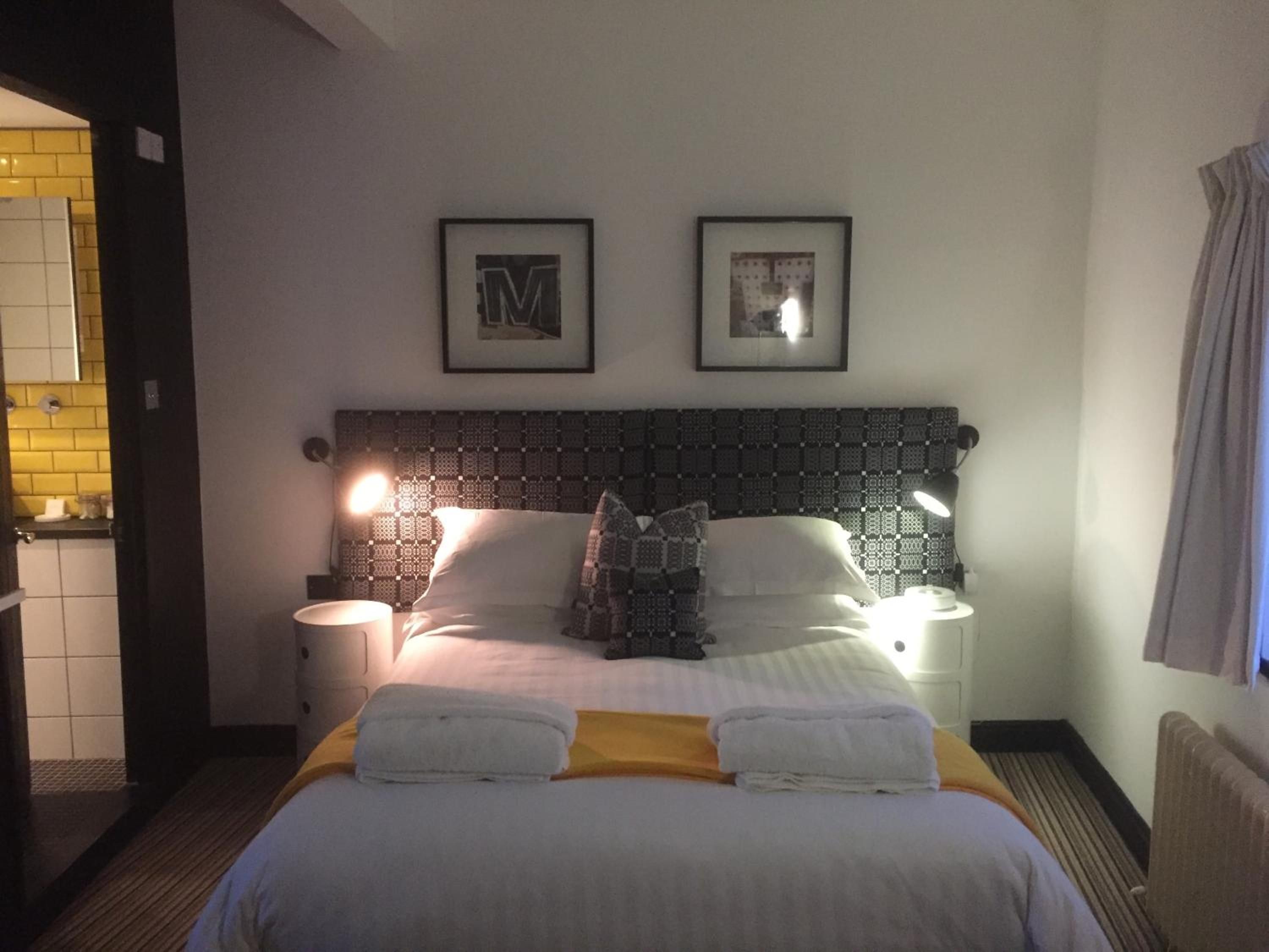 A hotel room with a bed, two bedside lamps, a headboard with a patterned design, and two framed pictures on the wall.