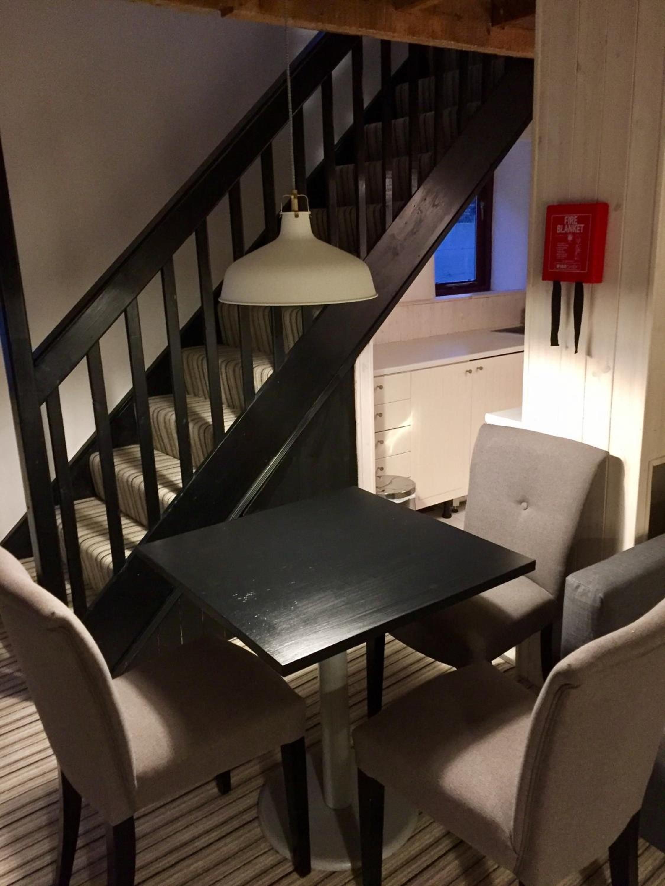 A staircase with a black railing, a white pendant light, and a small kitchenette area with a white cabinet and a red fire blanket.