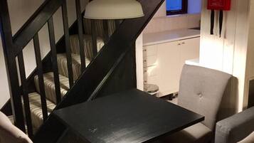 A staircase with a black railing, a white pendant light, and a small kitchenette area with a white cabinet and a red fire blanket.