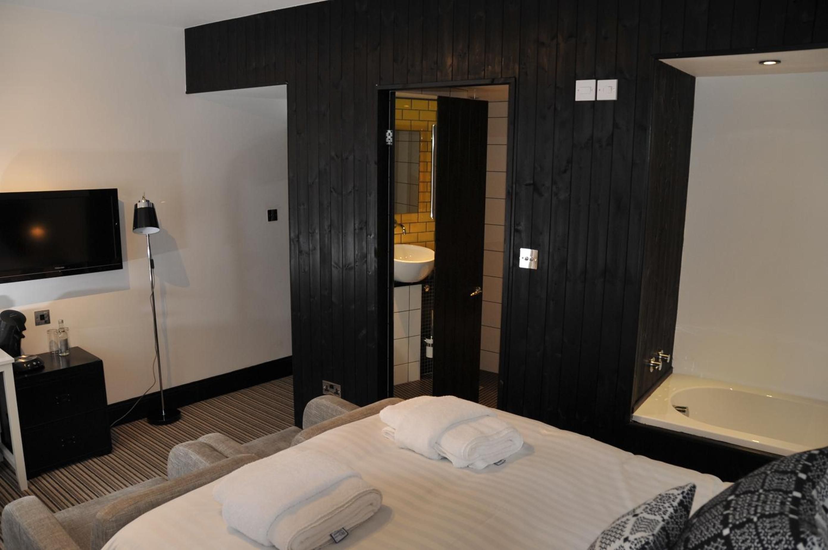 Habitación de hotel con cama, televisión, escritorio con lámpara y baño con bañera y lavamanos.