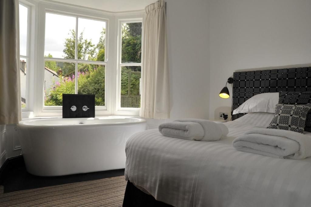 A hotel room with a large window, a bed with white linens, a black headboard, and a bedside lamp.