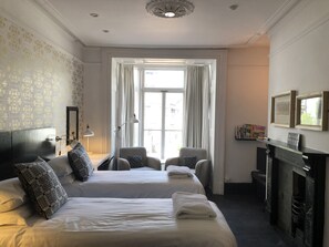 A hotel room with two beds, a sitting area with chairs, a fireplace, and a large window with curtains. - Greenbank Lodge Llangollen (Llangollen)