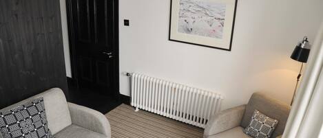 A room with two grey sofas, a framed picture on the wall, a radiator, and a door.