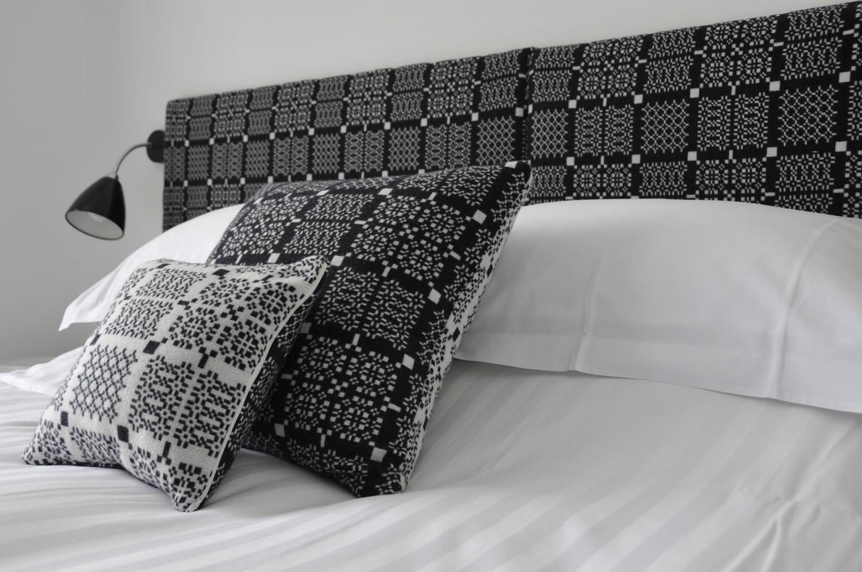 A bed with white bedding and two patterned pillows.