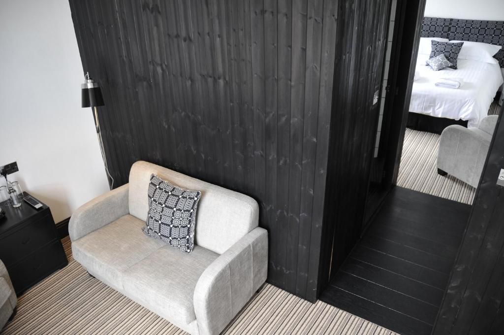 A hotel room with a grey sofa, a bedside table with a lamp, and a bed with a patterned headboard.
