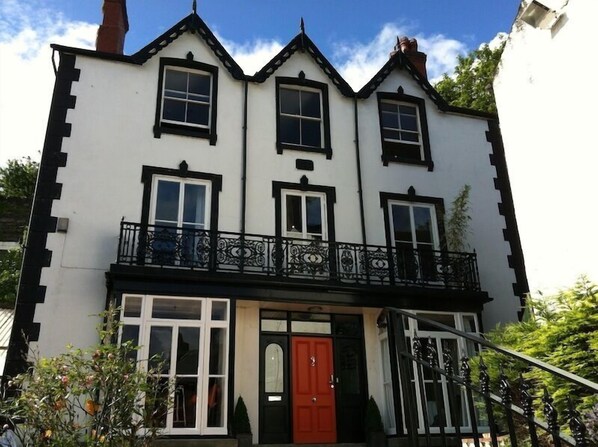 A three-story building with a black and white exterior, a red door, and a balcony with ornate black railings. - Greenbank Lodge Llangollen (Llangollen)