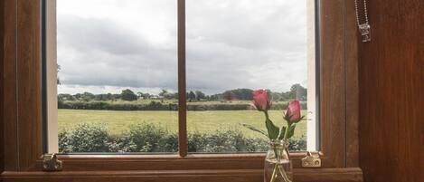 Eine hölzerne Fensterbank mit einer Vase, in der zwei Rosen stehen.