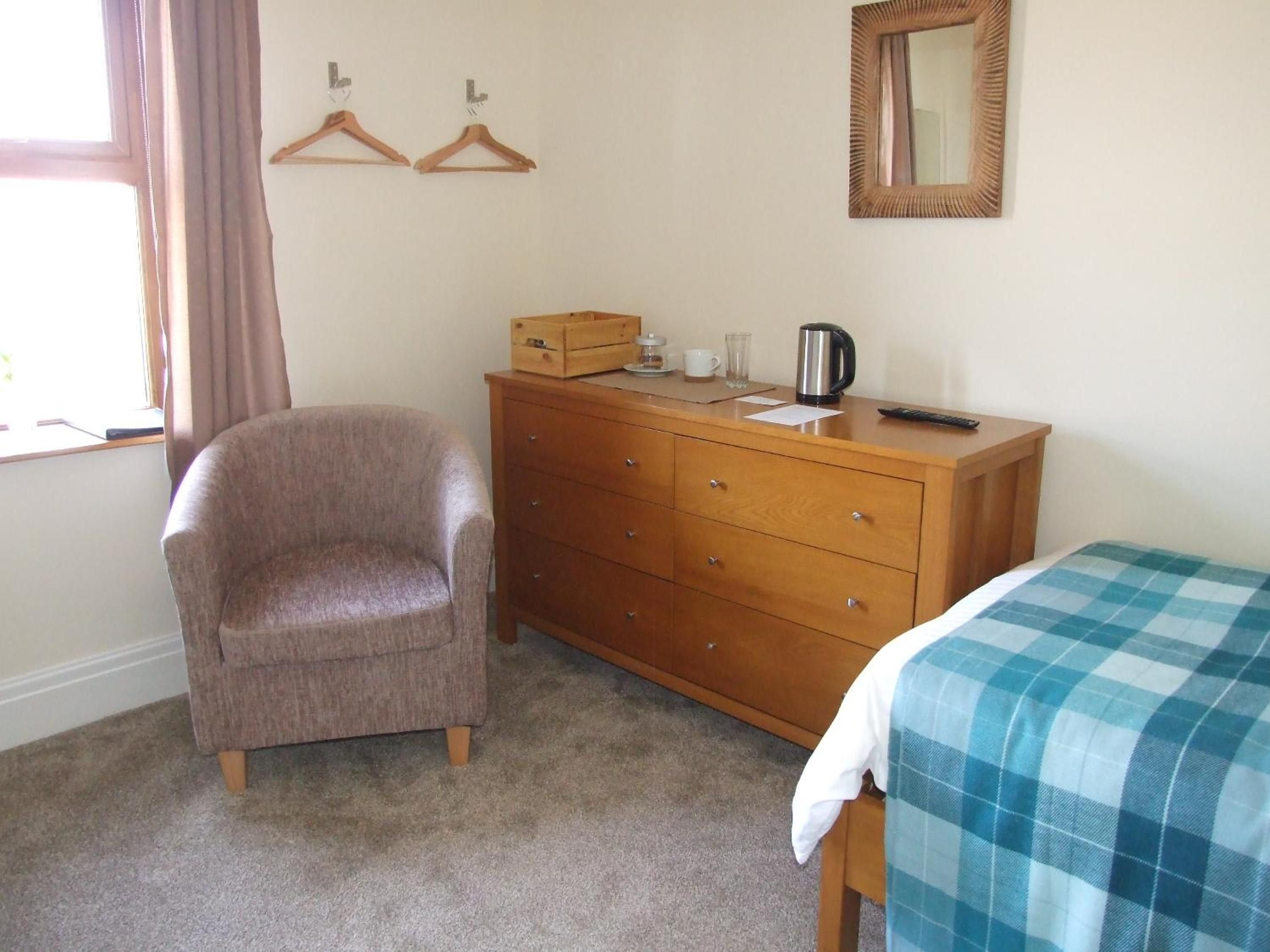 Ein Schlafzimmer mit einem Einzelbett, einem Holzschrank, einem Stuhl, einem Spiegel und einem Fenster mit Vorhängen.