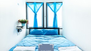 A bed with blue bedding and white towels, a potted plant, and a window with blue curtains. - Zee Thai Hostel (Bangkok)