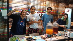 A group of people standing in front of a colorful mosaic wall with a table displaying food and drinks. - Zee Thai Hostel (Bangkok)