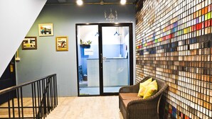 A reception area with a wicker sofa, a glass door entrance, and a wall with colorful tiles. - Zee Thai Hostel (Bangkok)
