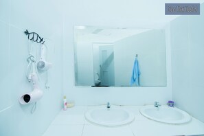A bathroom with two sinks, a mirror, and a hairdryer mounted on the wall.