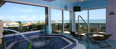 A hot tub area with a view of the sea, a TV, and lounge chairs.