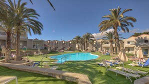 A pool area with lounge chairs and palm trees, surrounded by buildings with balconies. - Hotel LIVVO Koala Garden (San Bartolomé de Tirajana)