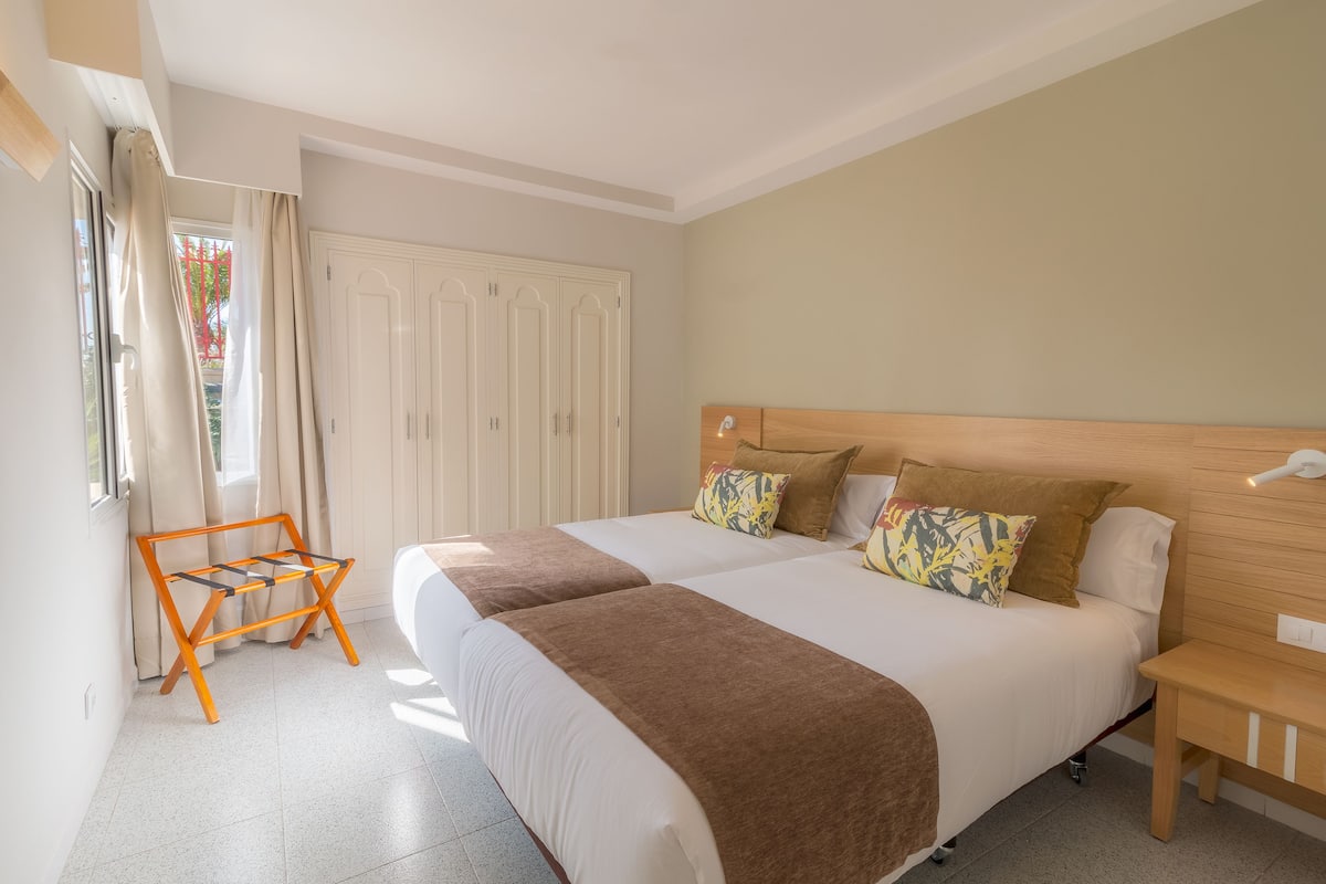 A double bed with a wooden headboard, two bedside tables, and a window with curtains.