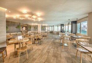 Tilava ravintola, jossa on puupöydät ja -tuolit, moderni kattovalaisin ja suuret ikkunat, joista tulee runsaasti luonnonvaloa.