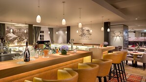 Una zona de bar con mostrador de madera, taburetes y lámparas colgantes.
