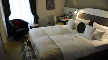 Ein Hotelzimmer mit einem großen Bett, einem kleinen Schreibtisch, einem Stuhl und einem Nachttisch mit einer Lampe.