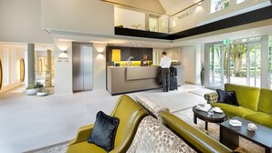 Un amplio vestíbulo con una mesa de recepción, un sofá verde y un sillón amarillo.