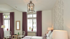A hotel room with a large bed, two bedside tables, a desk, a chair, a window with curtains, and a patterned wall. - Hotel Friedrichs (Schleiden)