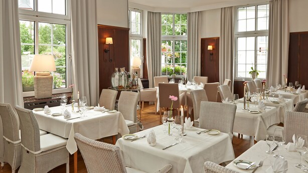 A dining area with multiple tables set for service, wicker chairs, and large windows with curtains. - Hotel Friedrichs (Schleiden)