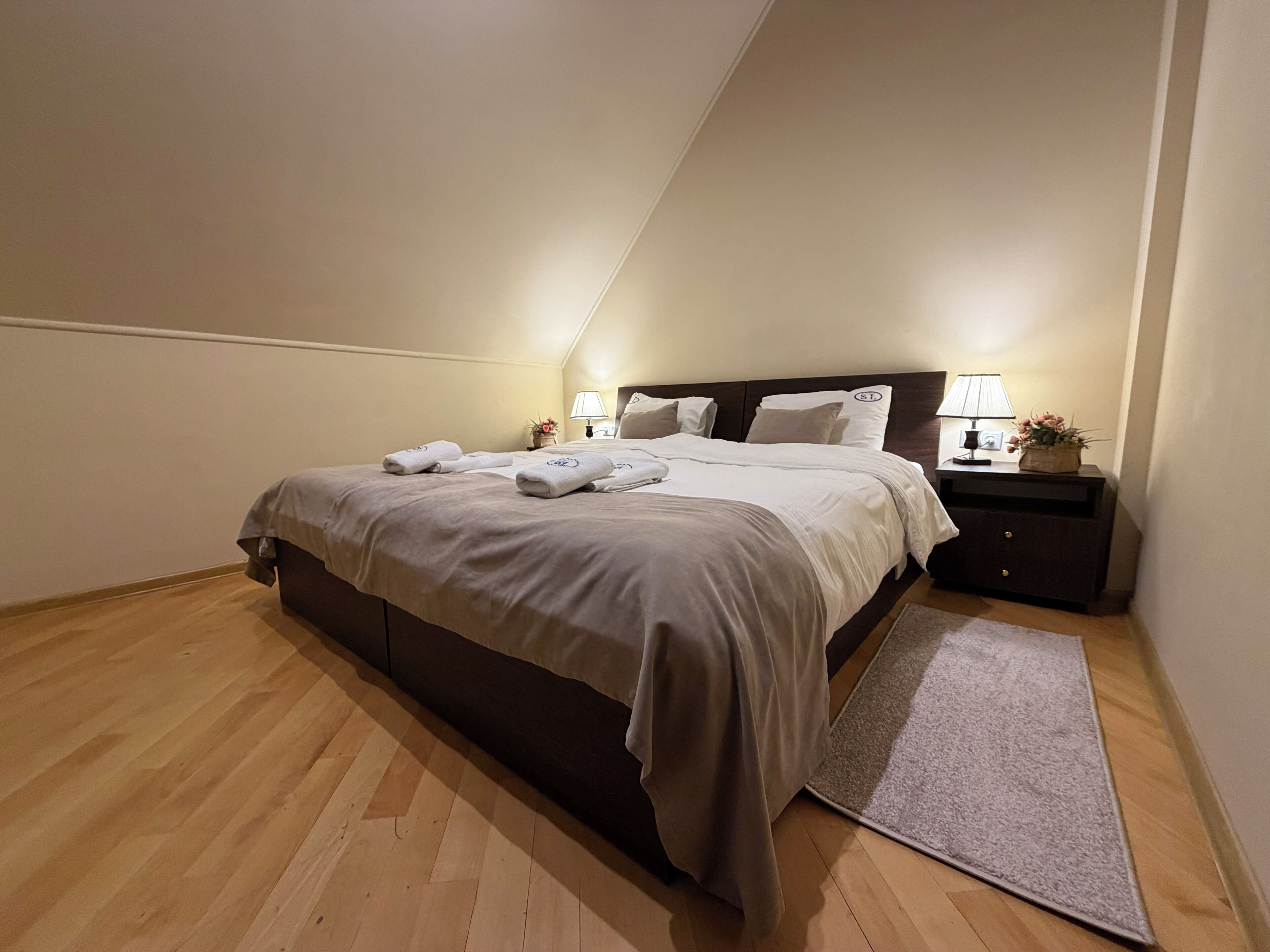 A neatly made bed with pillows and a bedside table with a lamp and a vase of flowers.