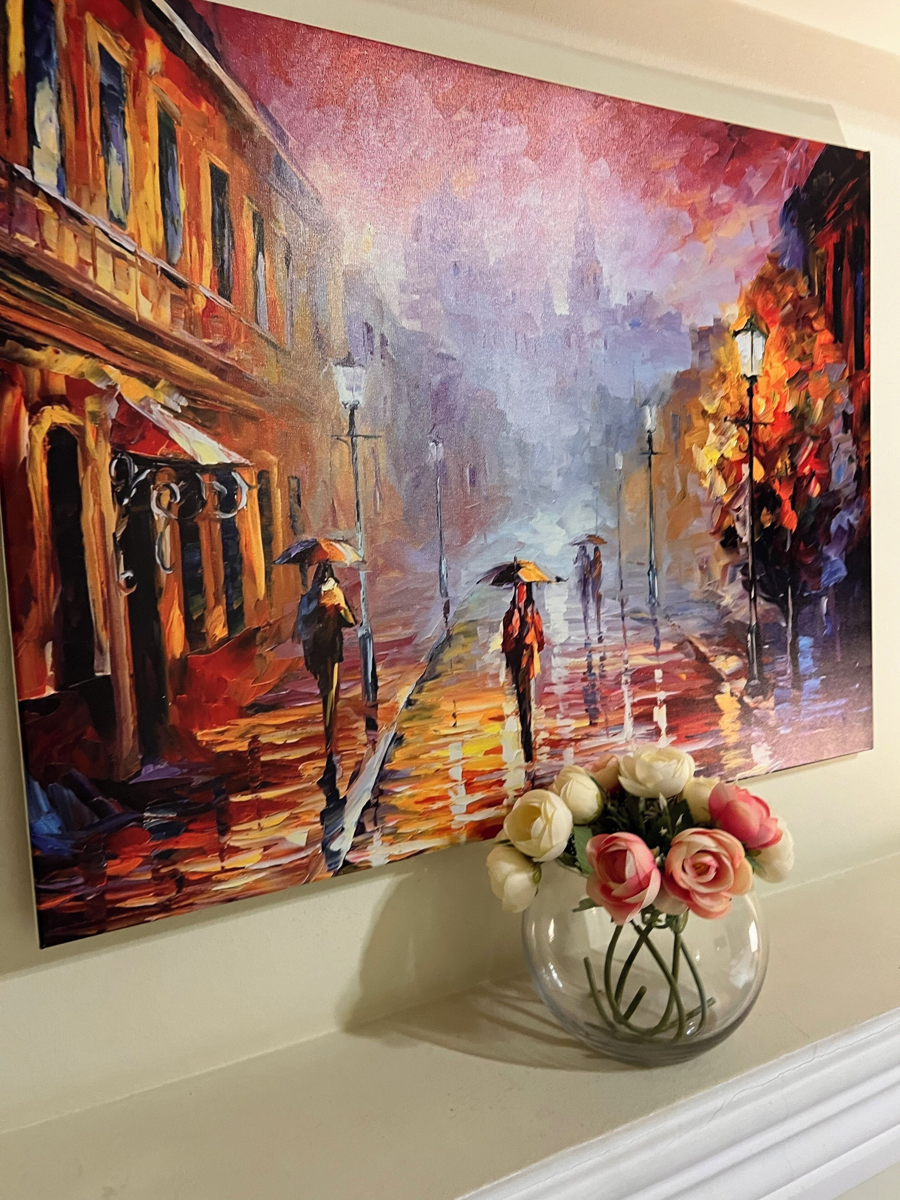 A painting of a street scene with people holding umbrellas, a vase with flowers, and a building with a red facade.