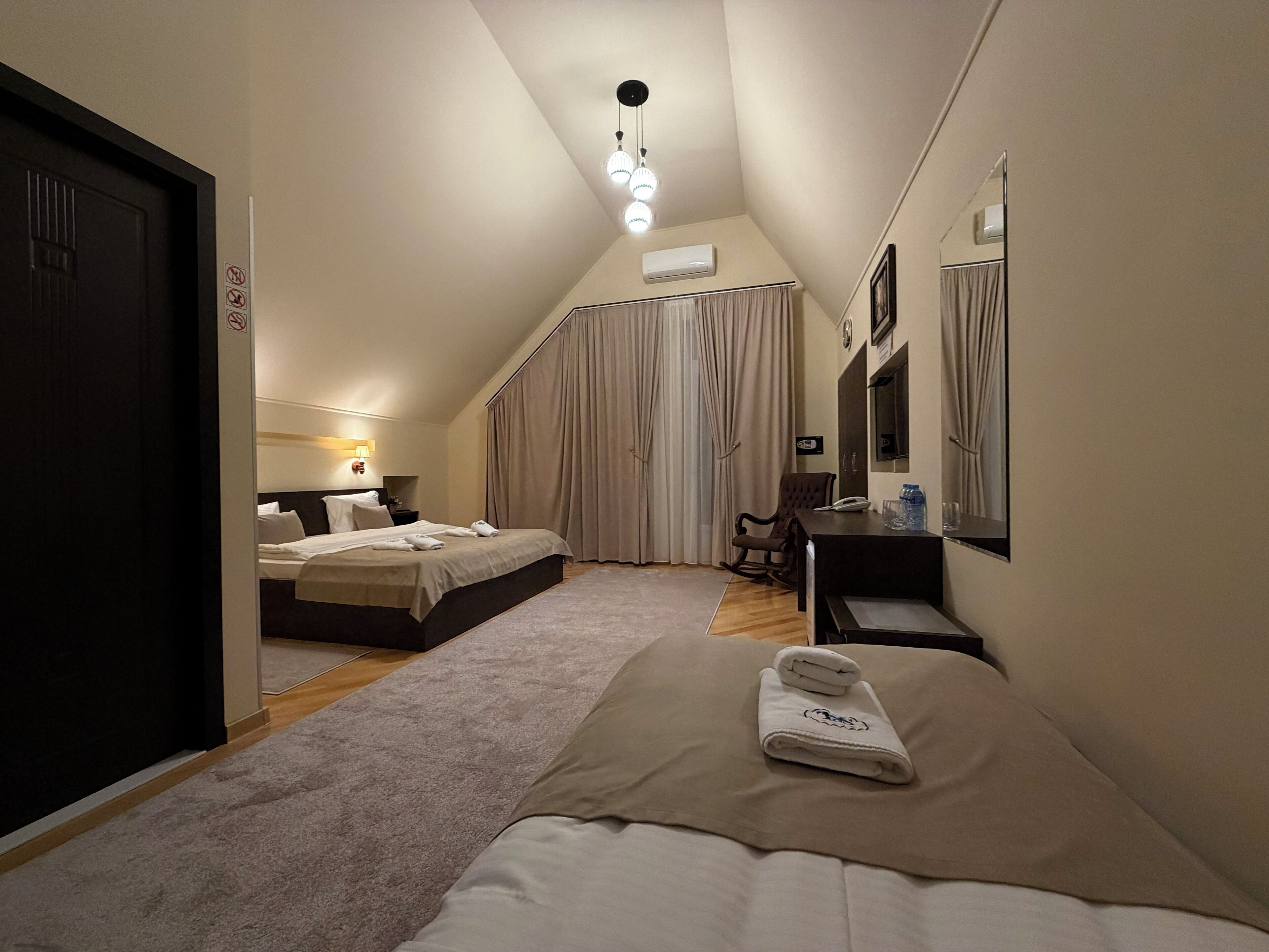 Ein Hotelzimmer mit Bett, Schreibtisch, Stuhl, Spiegel und einem Fenster mit Vorhängen.