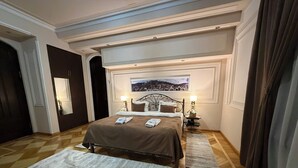 A hotel room with a bed, two bedside tables, a nightstand, a window with a cityscape view, and a door. - S&L Boutique Hotel  (Tbilisi)