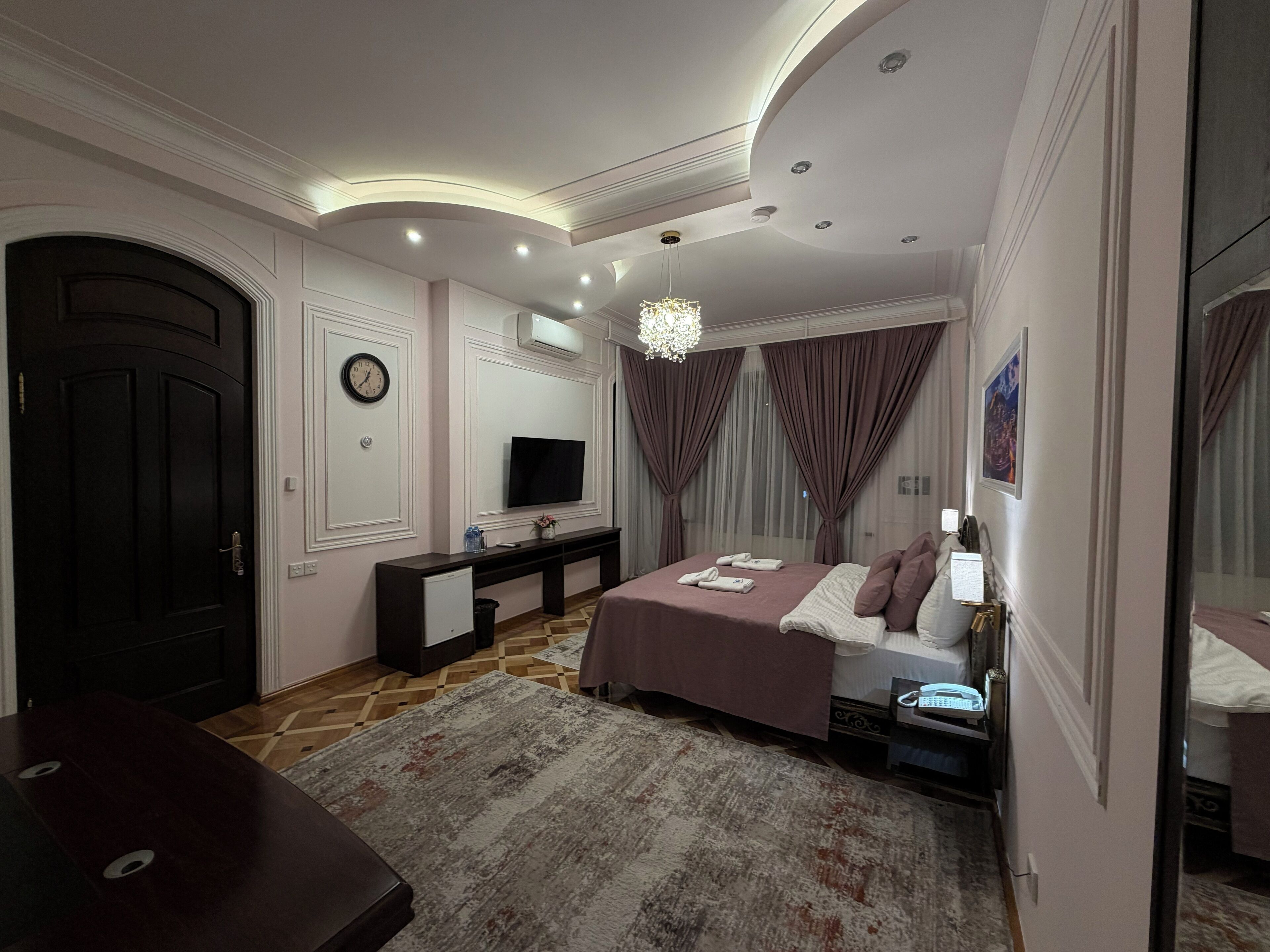 A bedroom with a bed, bedside table, TV, and a large mirror.