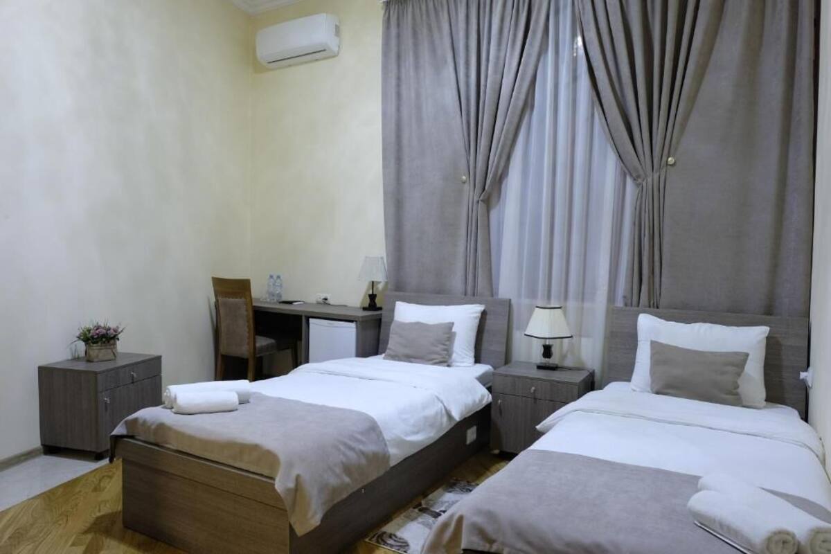 A hotel room with two beds, a desk, a chair, a small table, and a nightstand.