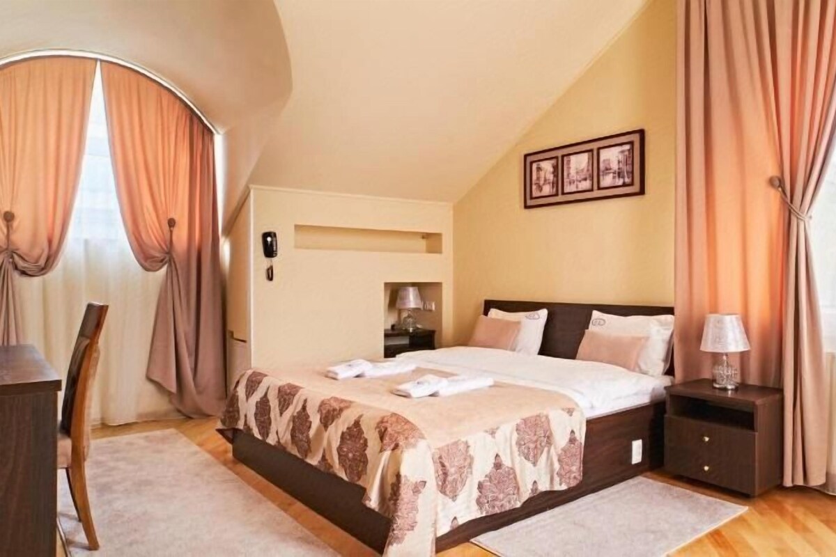 A bedroom with a bed, bedside tables, a desk, and curtains.