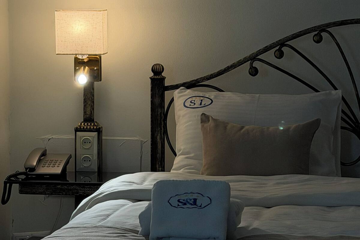 A neatly made bed with a pillow and a folded towel, a bedside lamp, and a telephone on a bedside table.