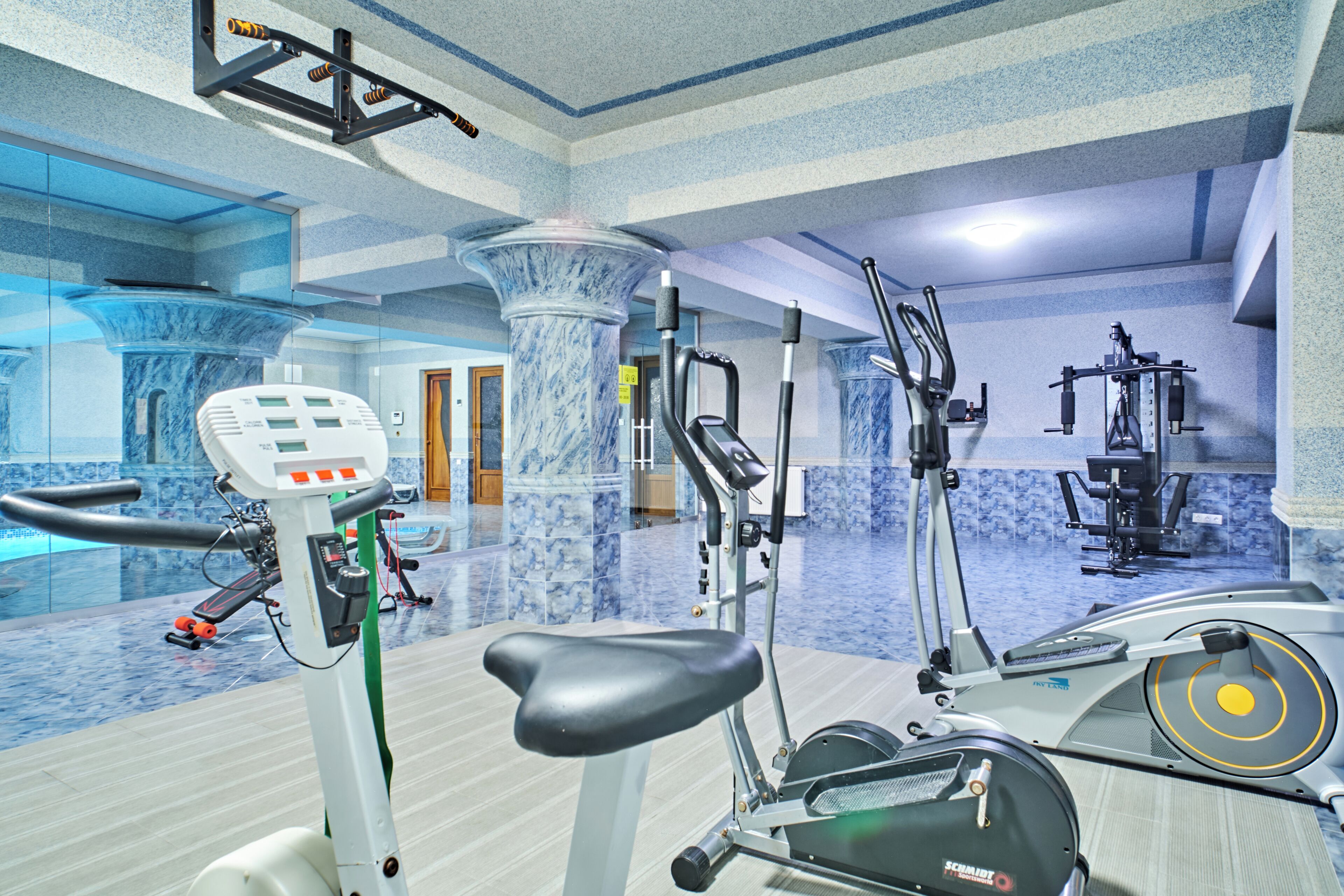 A gym with exercise equipment, a marble column, and a pool area.