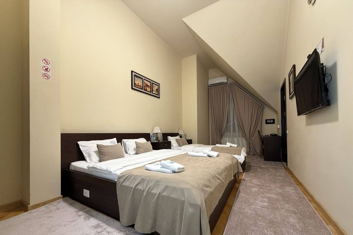 A hotel room with a large bed, a desk, a chair, a TV, and a window with curtains.