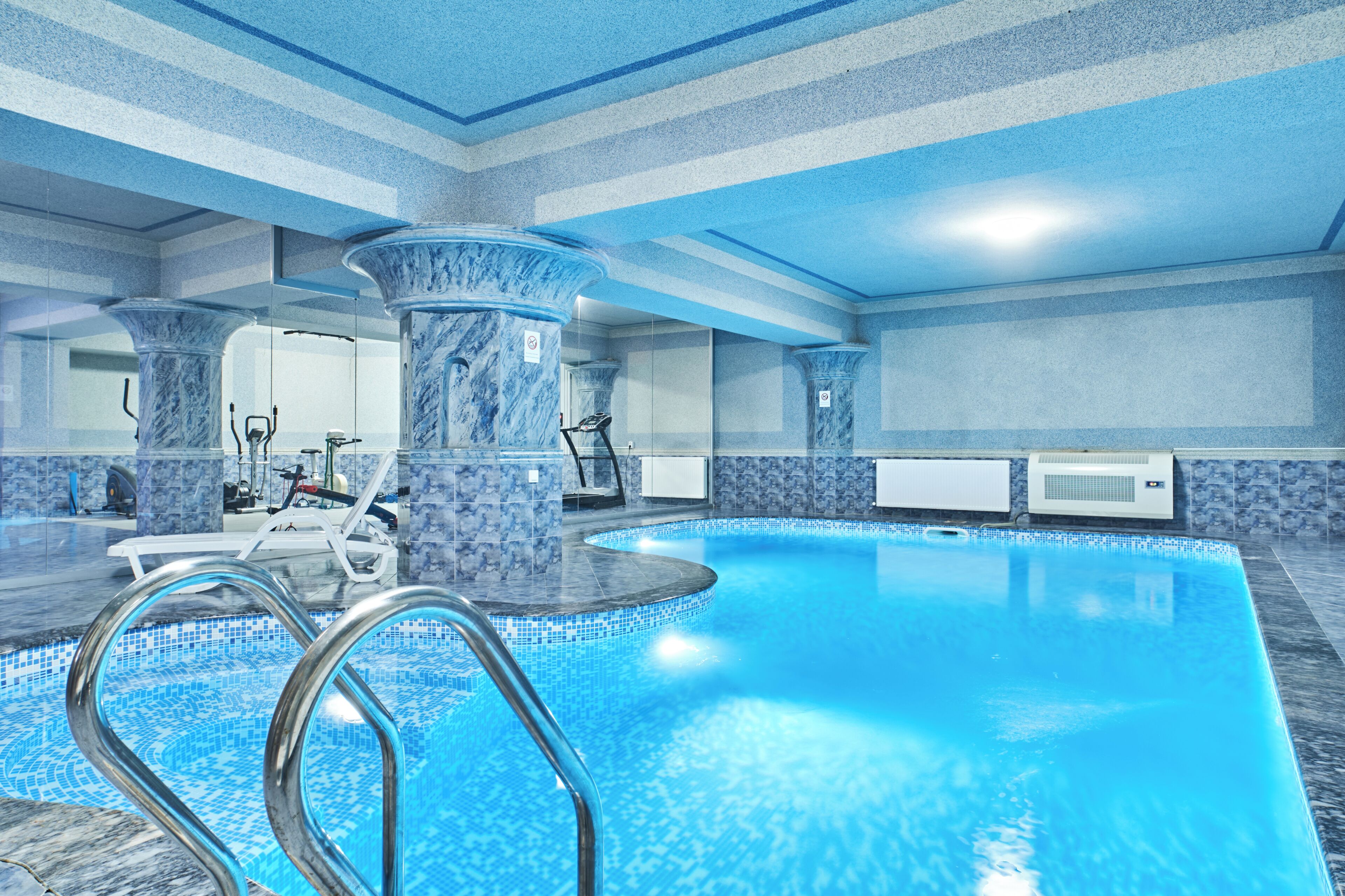An indoor swimming pool with a clear water surface, surrounded by marble columns and a tiled floor.