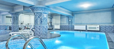 Una piscina interior con superficie de agua cristalina, rodeada de columnas de mármol y suelo de baldosas.
