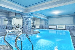 Una piscina interior con superficie de agua cristalina, rodeada de columnas de mármol y suelo de baldosas.