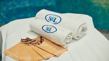 A neatly folded white towel with embroidered initials on a bed, accompanied by several orange pamphlets.