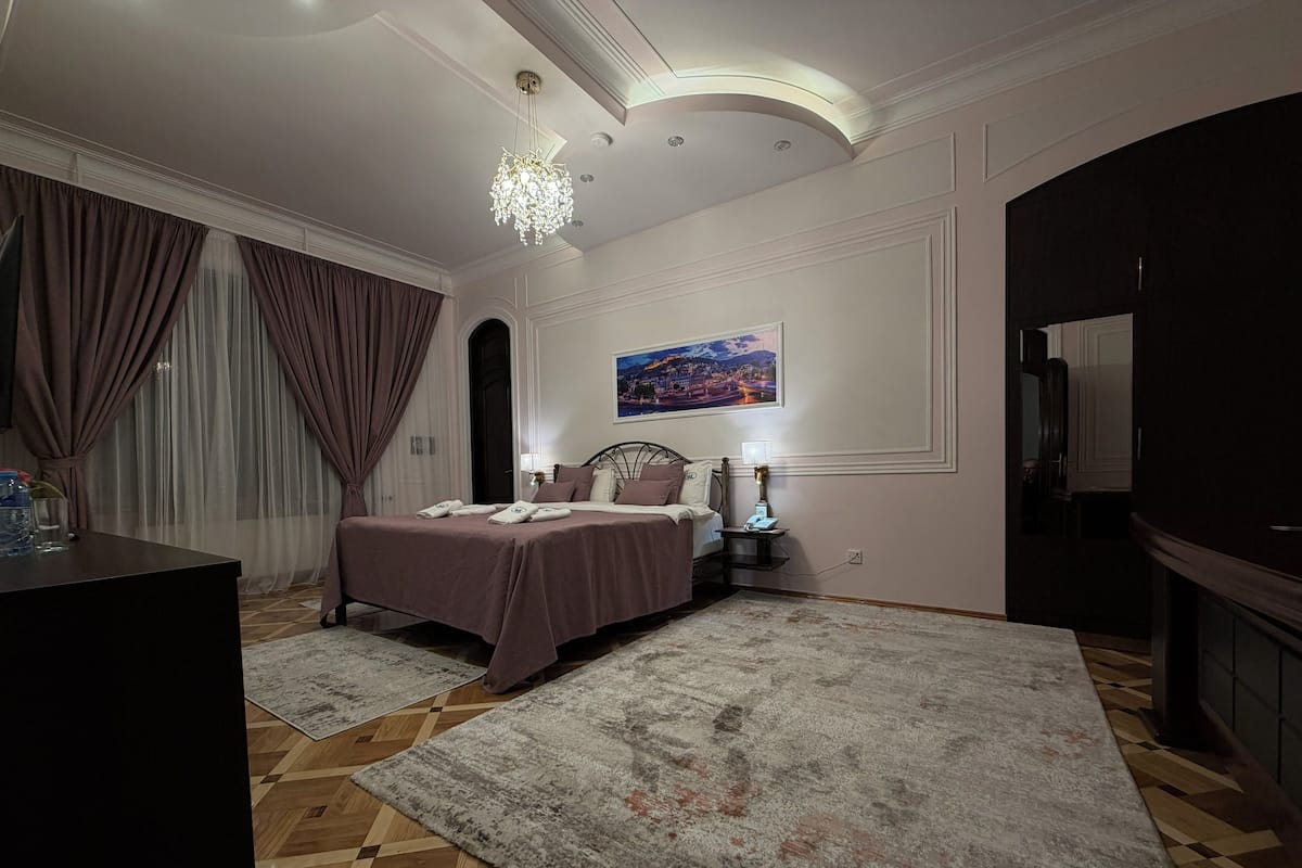 A bedroom with a bed, bedside table, lamp, and a painting on the wall.