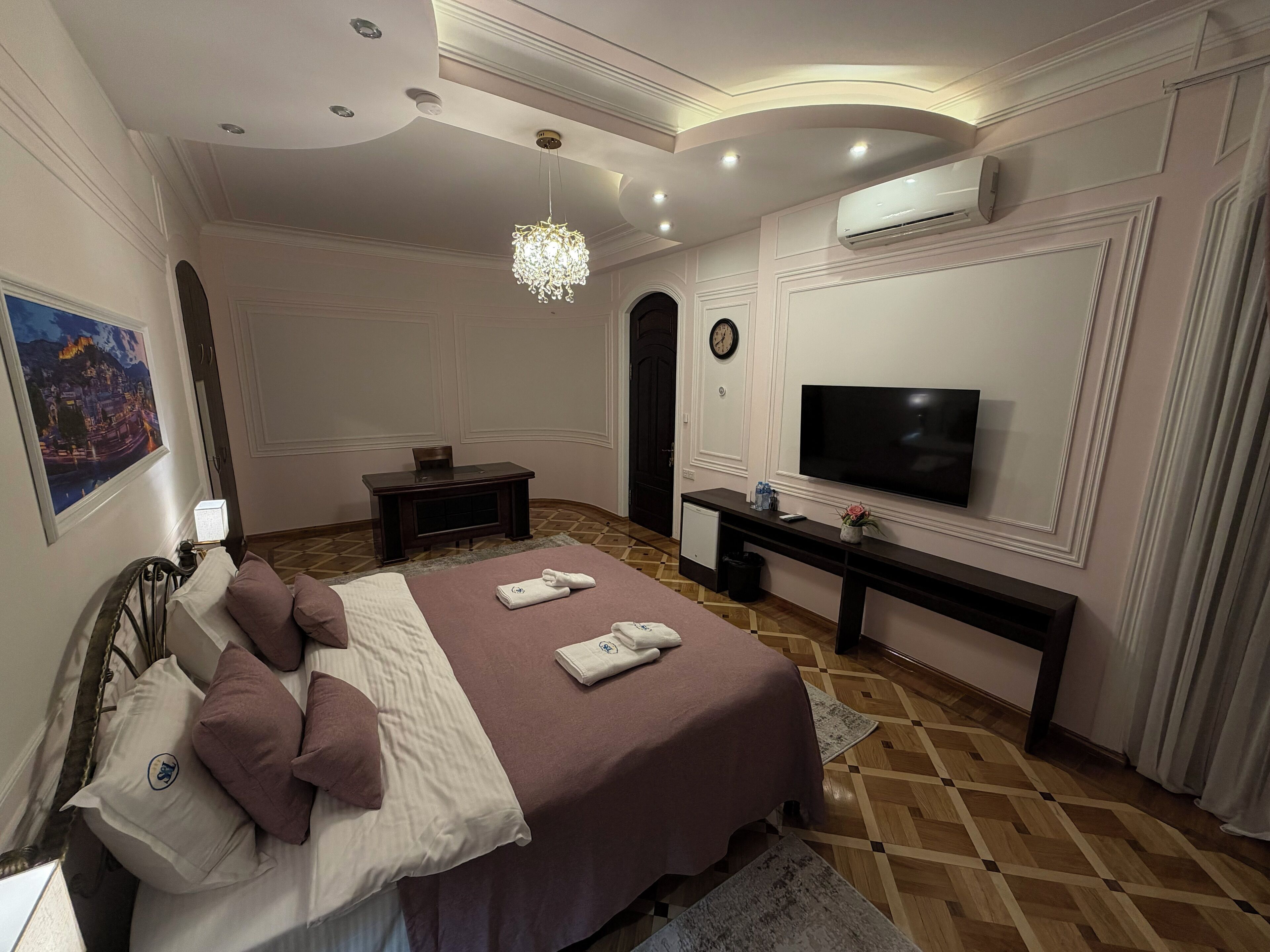 A bedroom with a bed, a TV, a desk, and a wall-mounted air conditioner.