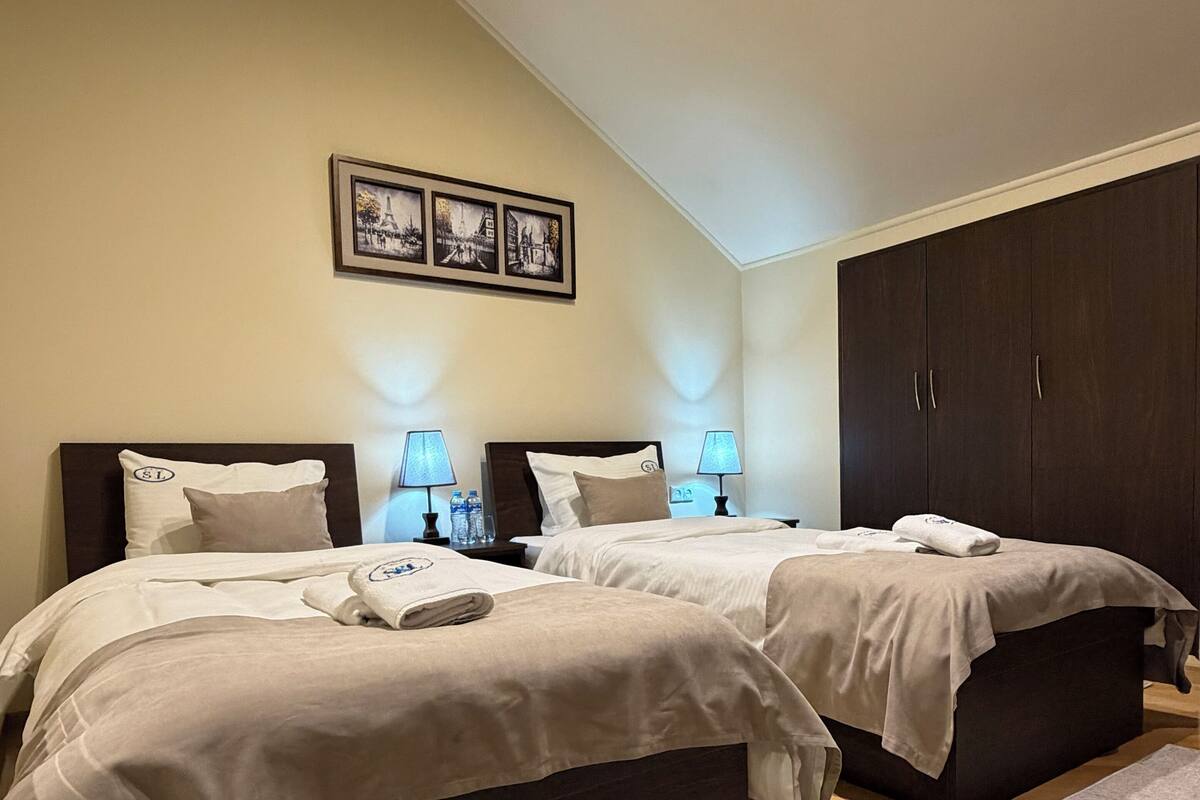 A bedroom with two beds, a dark wardrobe, and a framed picture on the wall.