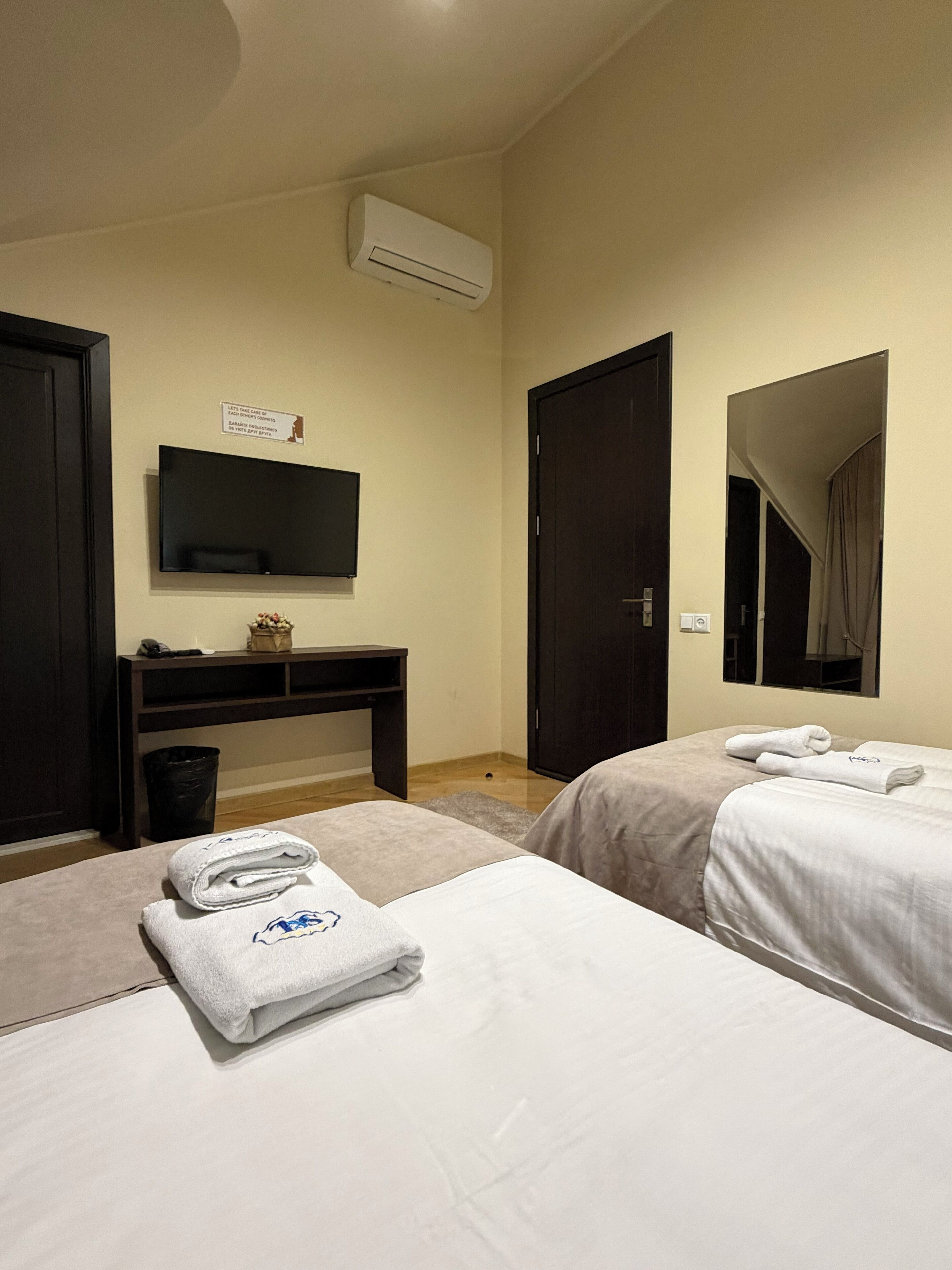 Ein Hotelzimmer mit zwei Betten, einem Schreibtisch, einem Fernseher und einer Klimaanlage.