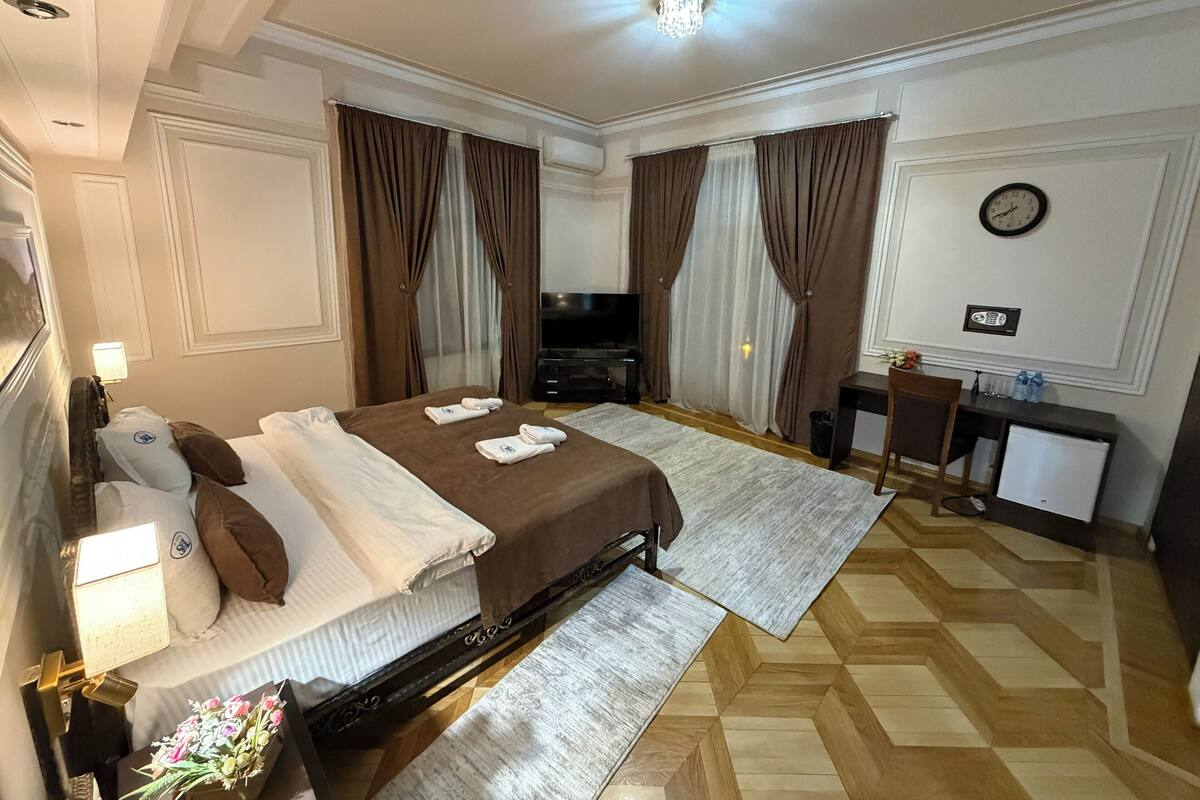 A hotel room with a bed, a desk, a television, and a clock on the wall.